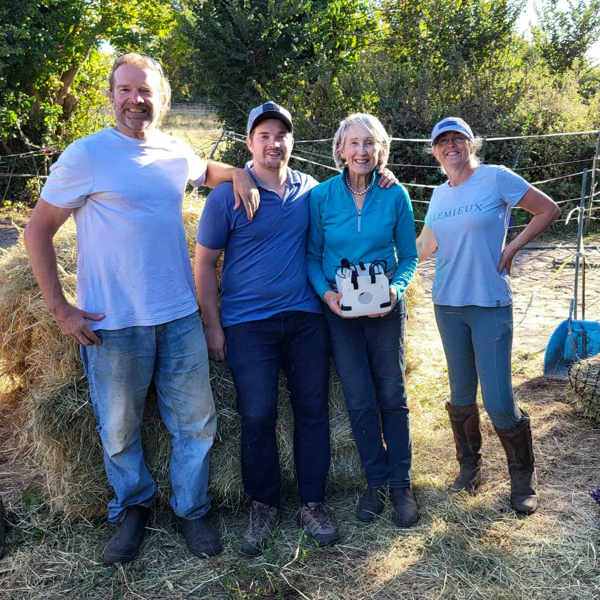 Four people standing in a field with hay and straw, smiling at the camera.